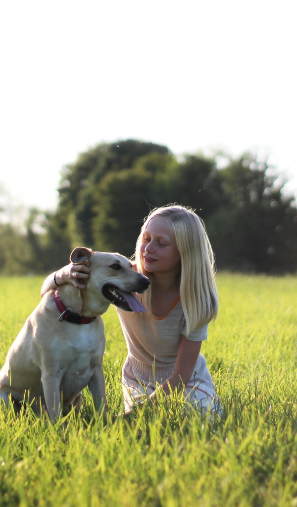 Маленькая девочка с собакой в зеленой траве