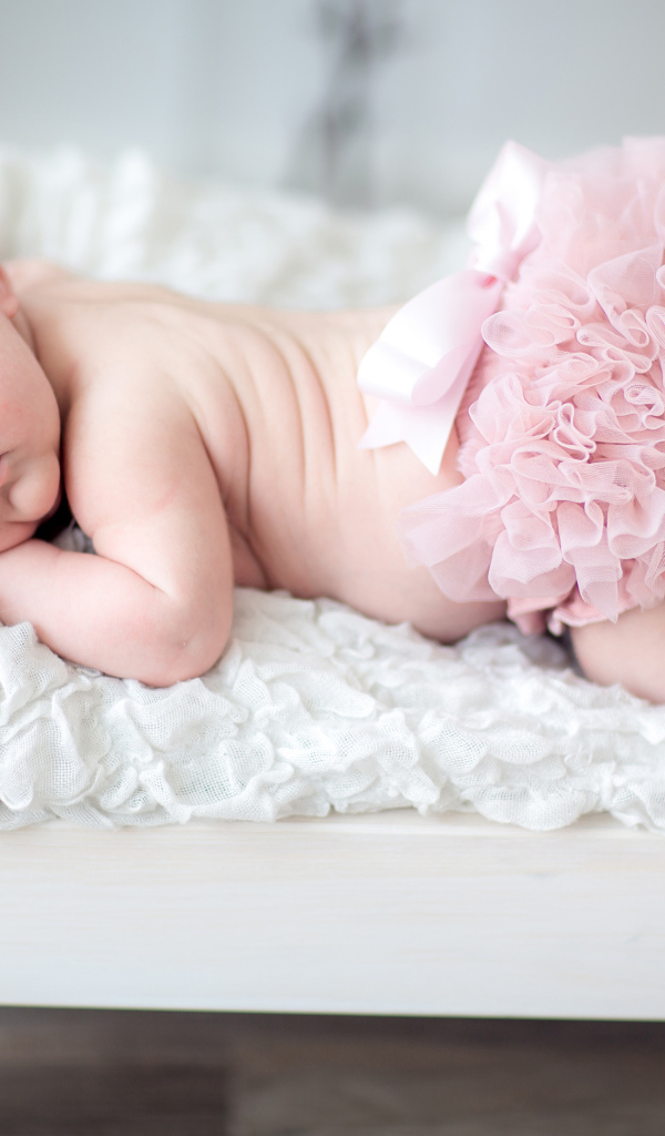 Маленькая спящая девочка в розовом костюме в кроватке