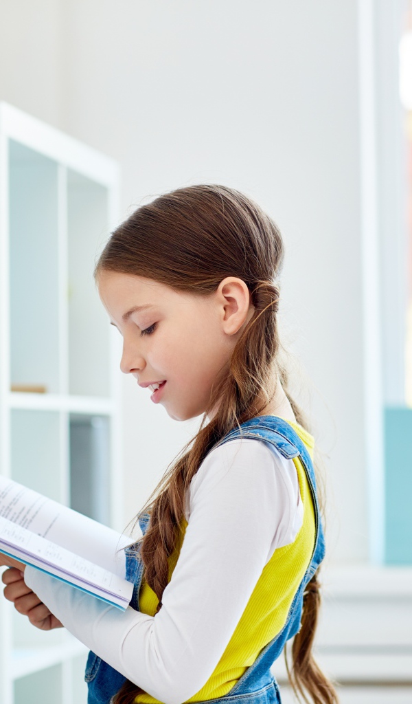 Умная девочка школьница с книгой в библиотеке 