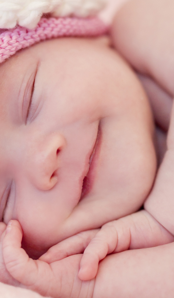 Улыбающийся грудной ребенок в розовой вязаной шапке 