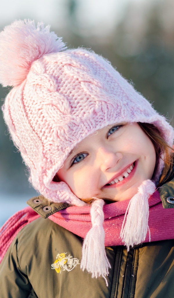 Улыбающаяся девочка в розовой шапке зимой