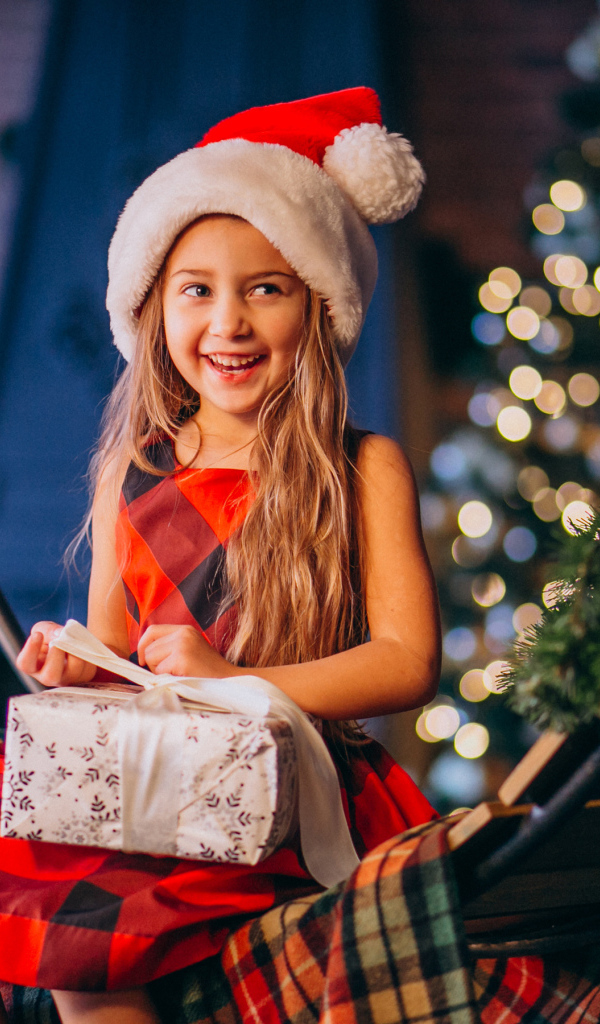 Улыбающаяся девочка сидит с подарком на Рождество 