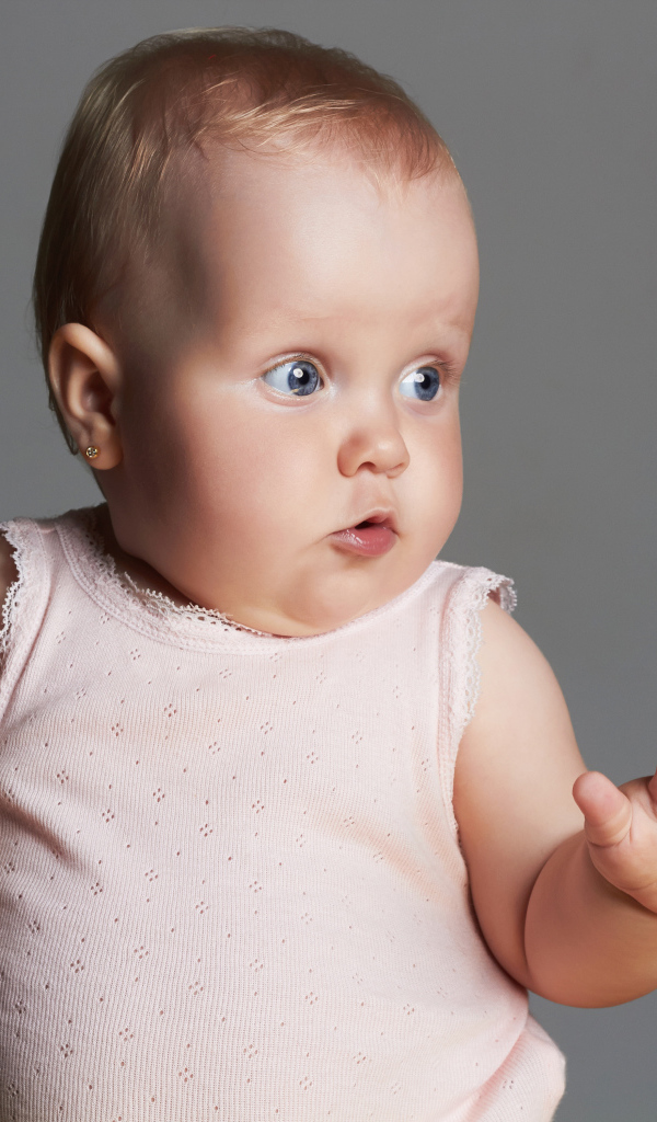 Удивленный маленький ребенок на сером фоне