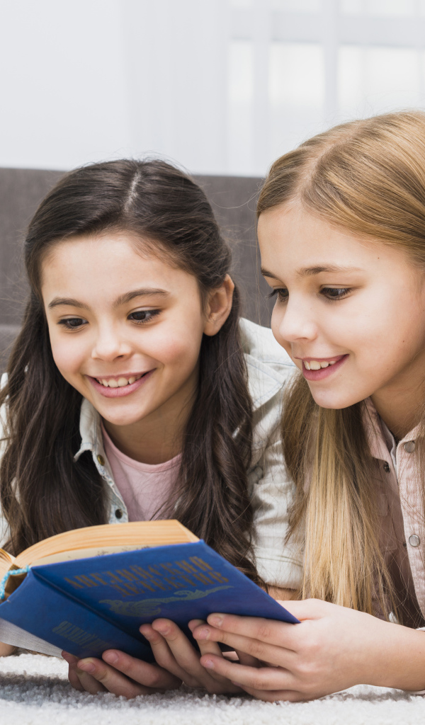 Две маленькие девочки читают книгу на полу