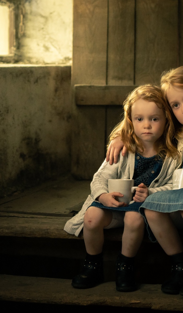 Две маленькие сестры пьют какао на ступеньках дома
