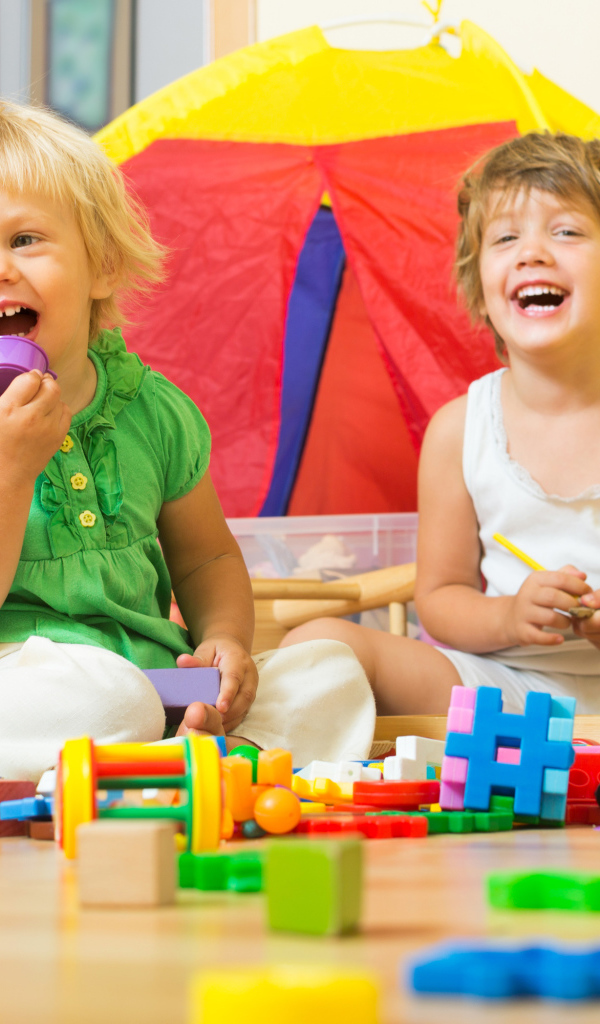 Два улыбающихся ребенка играют с конструктором 