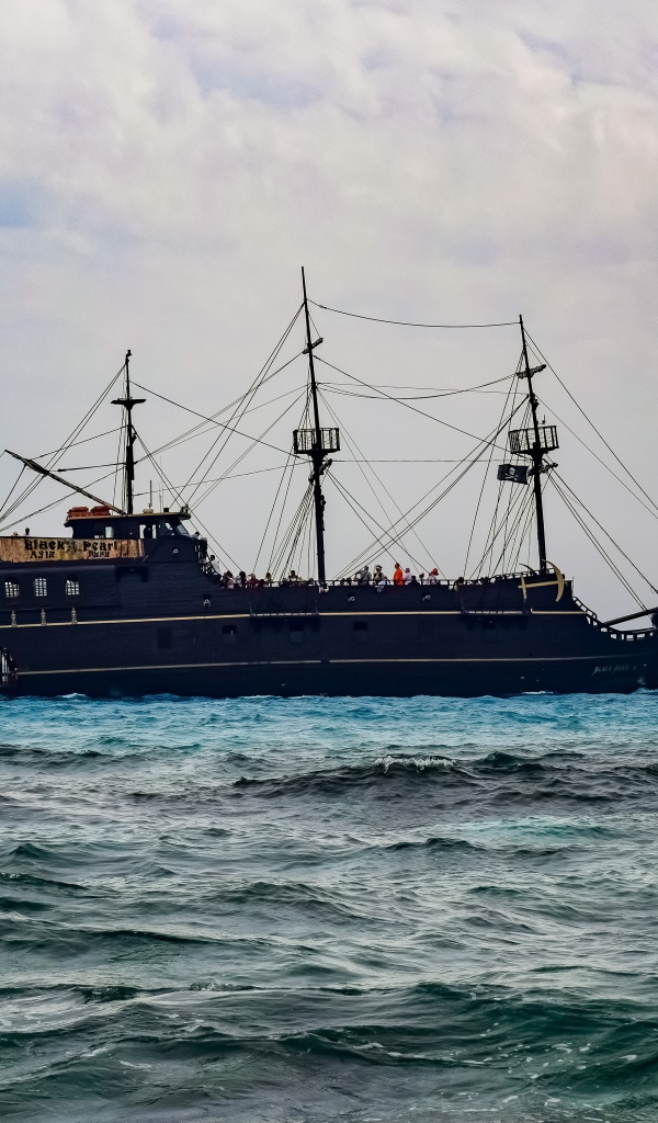 Большой черный пиратский корабль с опущенными парусами в море 