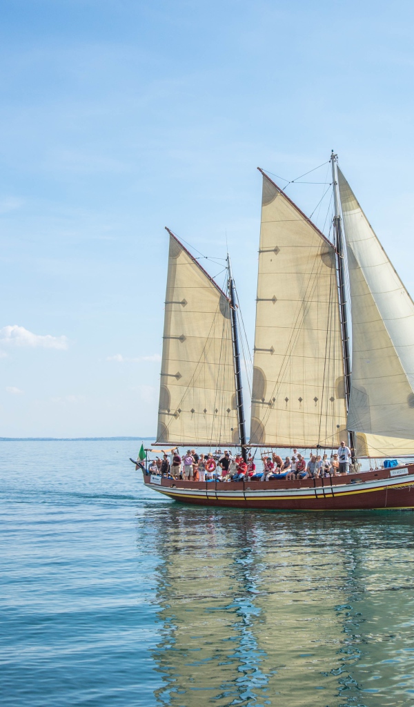 Судно с белыми парусами в море на фоне голубого неба 