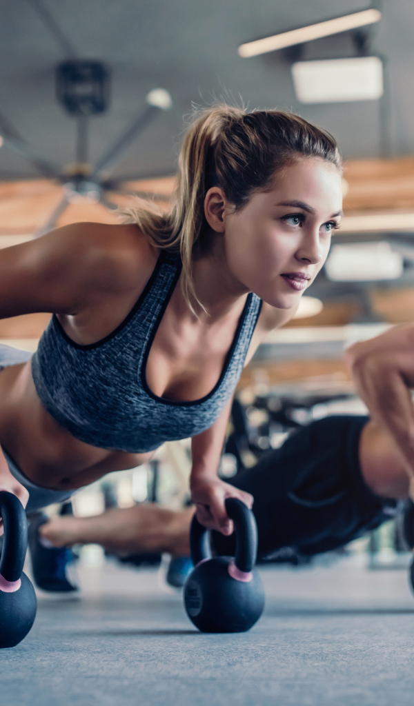 Парень и девушка занимаются с гирями в спортзале 