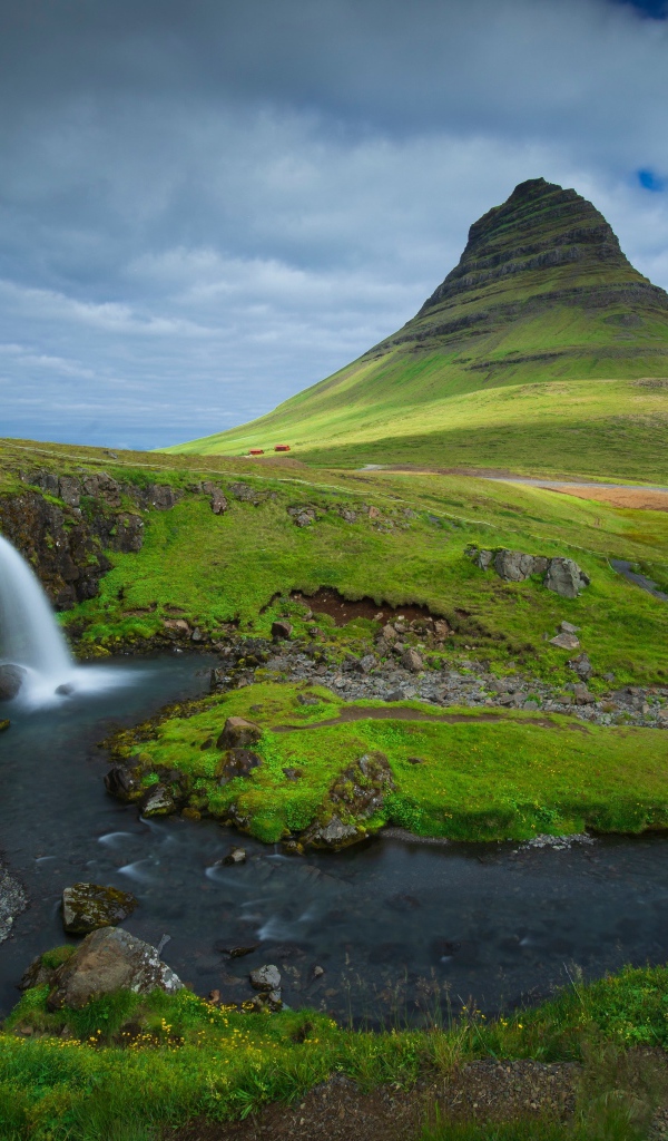 Вид на маленький водопад и покрытую зеленью гору, Исландия