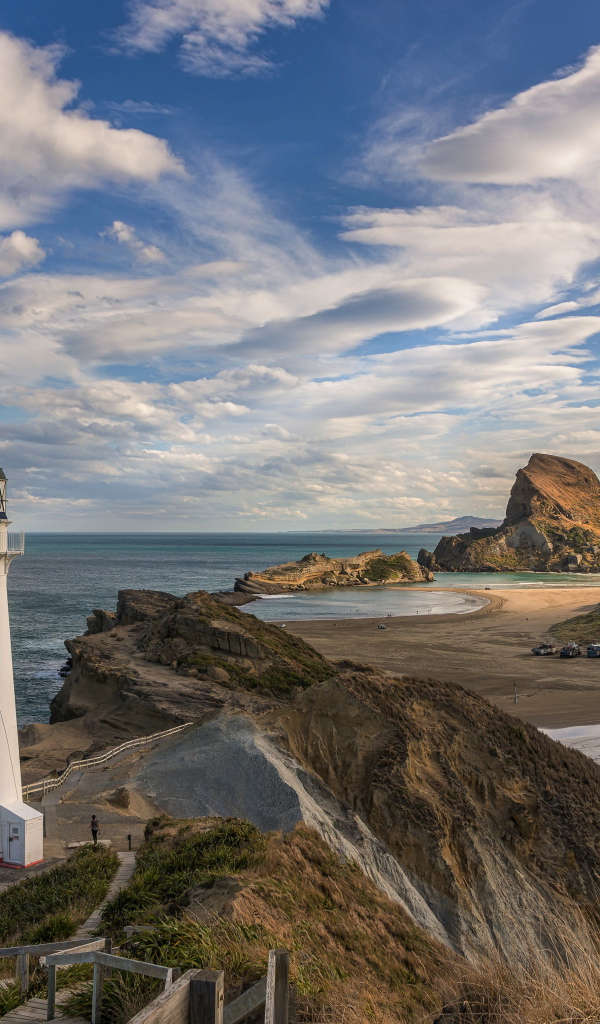 Маяк на скалистом берегу под голубым небом с белыми облаками у моря, Новая Зеландия 