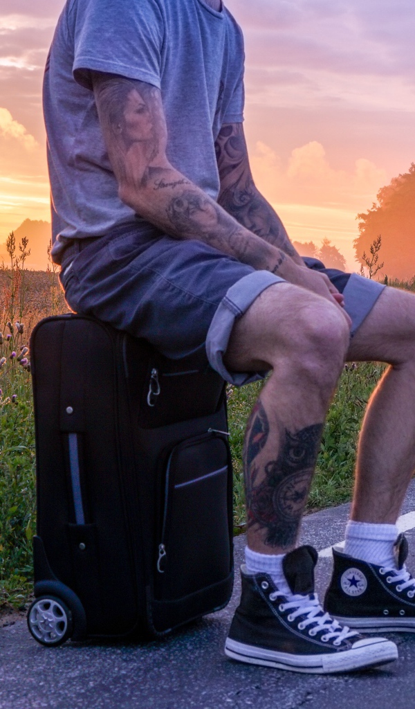 Мужчина с татуировками на теле сидит на чемодане 
