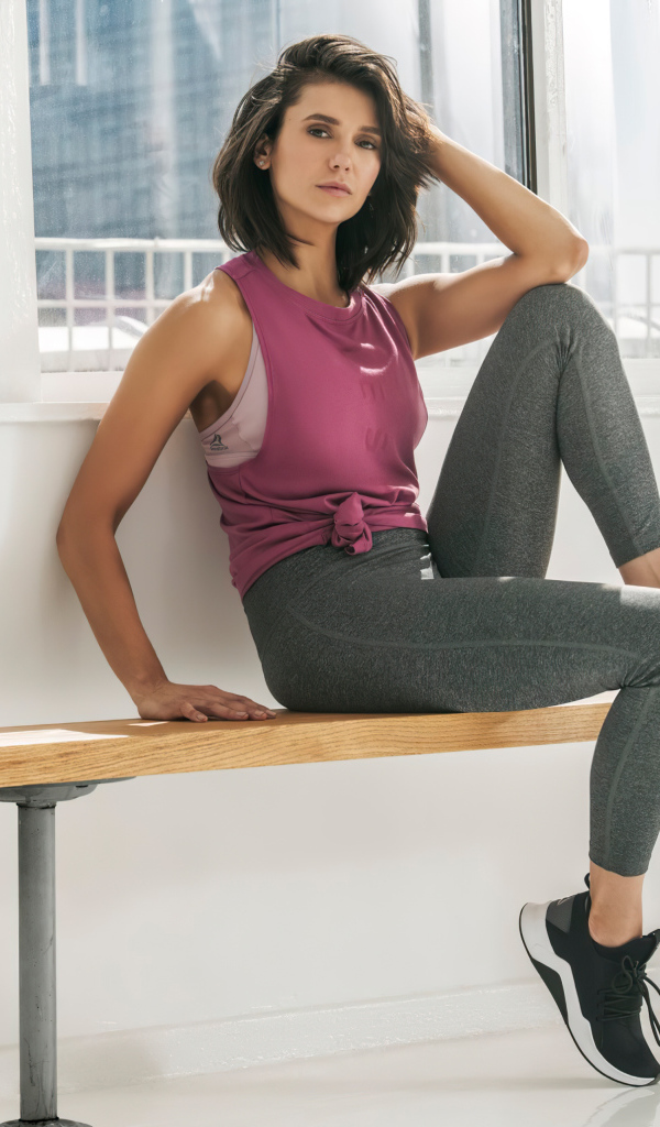 Актриса Нина Добрев сидит на лавке в спортивном костюме