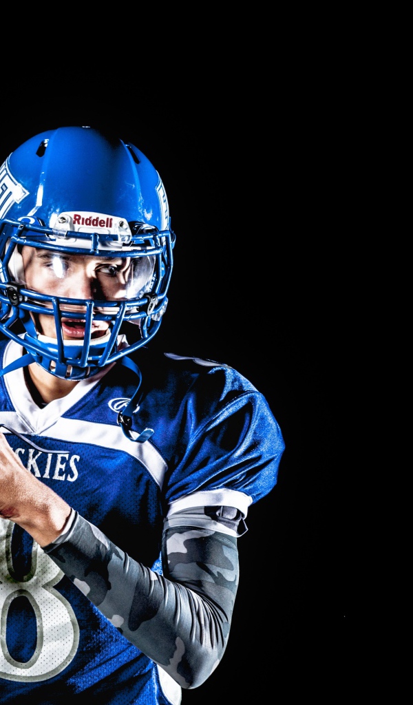 Игрок в американский футбол с мячом в руках на черном фоне 