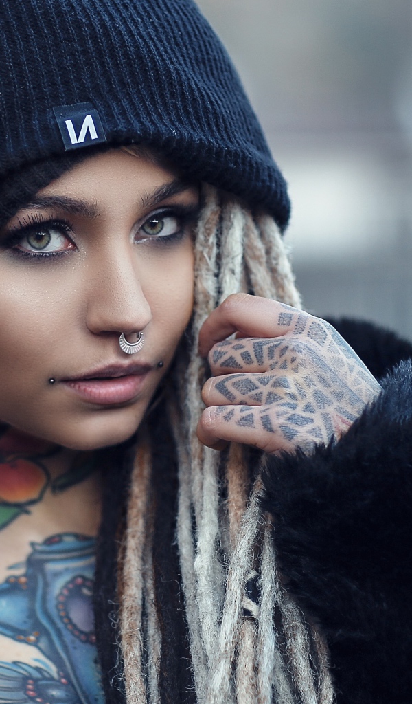 Красивая девушка в черной шапке с татуировками на теле 