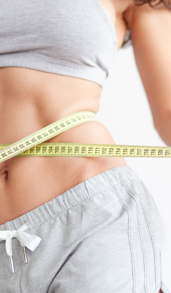 Красивая стройная девушка меряет талию сантиметром 