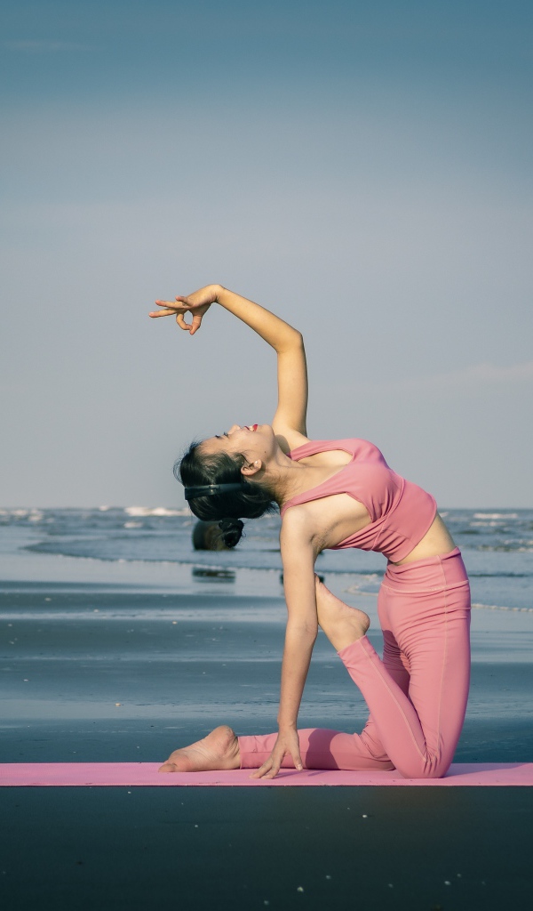 Девушка занимается йогой у моря 