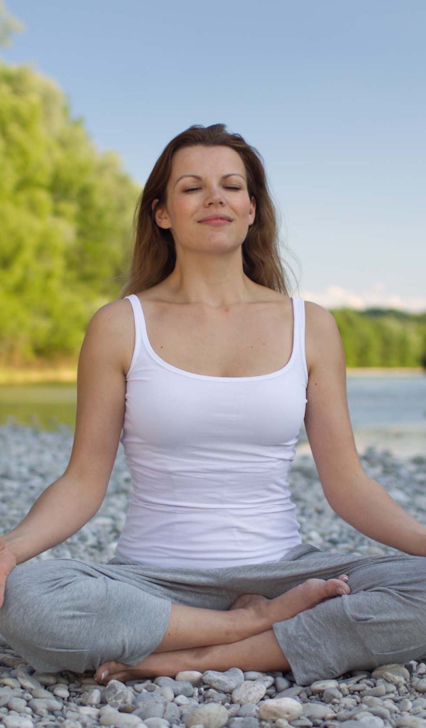 Девушка в позе лотоса медитирует у реки 