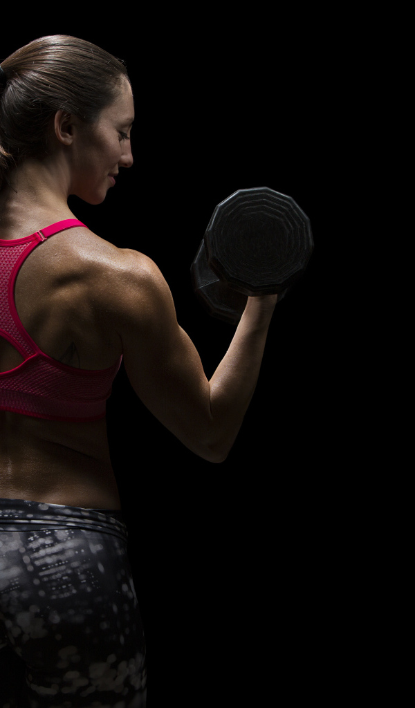 Девушка качает руки гантелей на черном фоне 