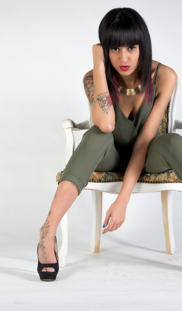 Girl with tattoos on her body sits on a chair