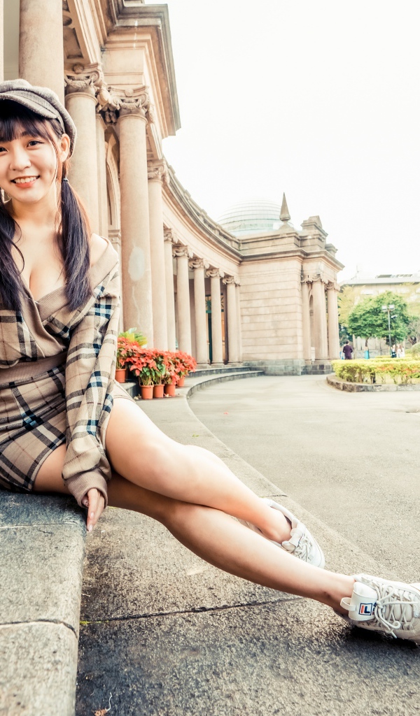 Улыбающаяся азиатка в кепке сидит на ступеньках 