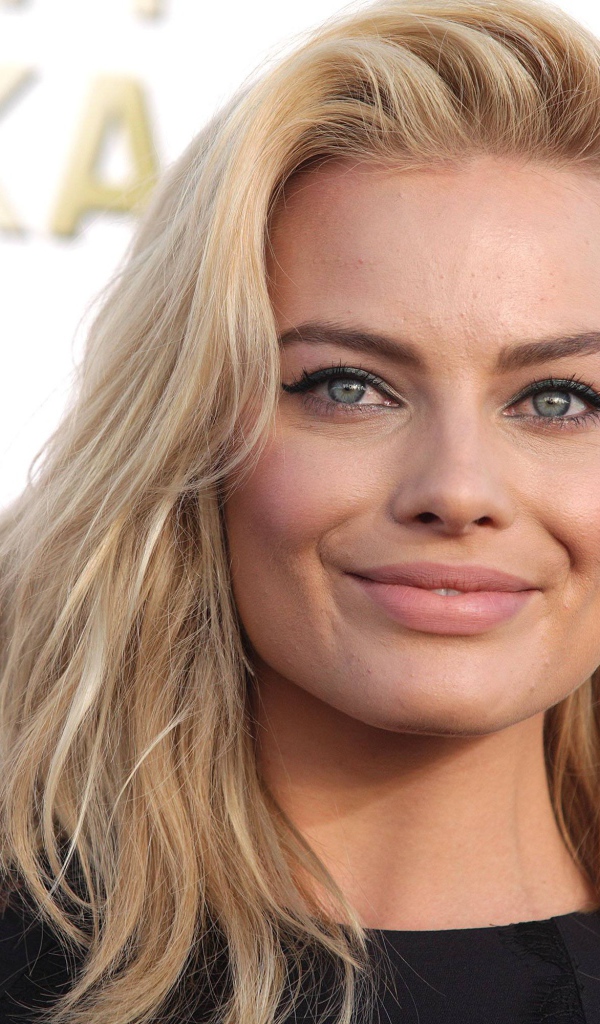 Улыбающаяся блондинка, актриса Марго Робби у стены