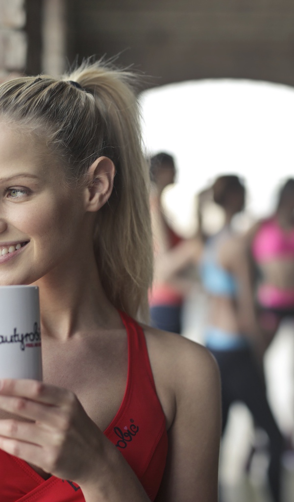 Улыбающаяся спортивная девушка с чашкой кофе у окна