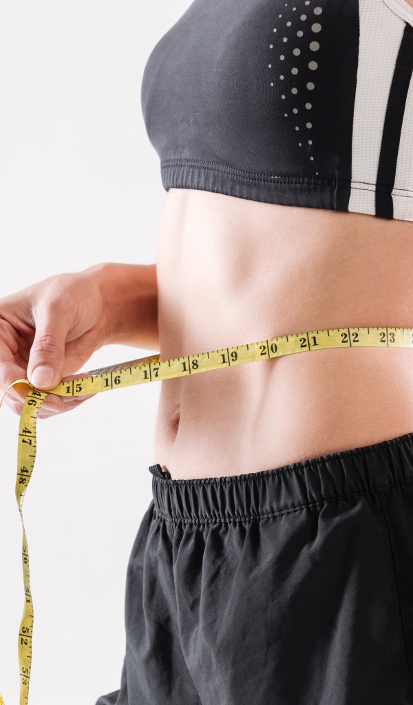 Спортивная девушка меряет талию сантиметром 