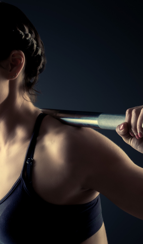 Спортивная девушка занимается со штангой в спортзале на сером фоне