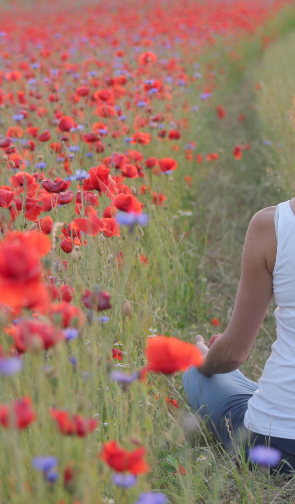 Молодая девушка медитирует на поле с красными маками