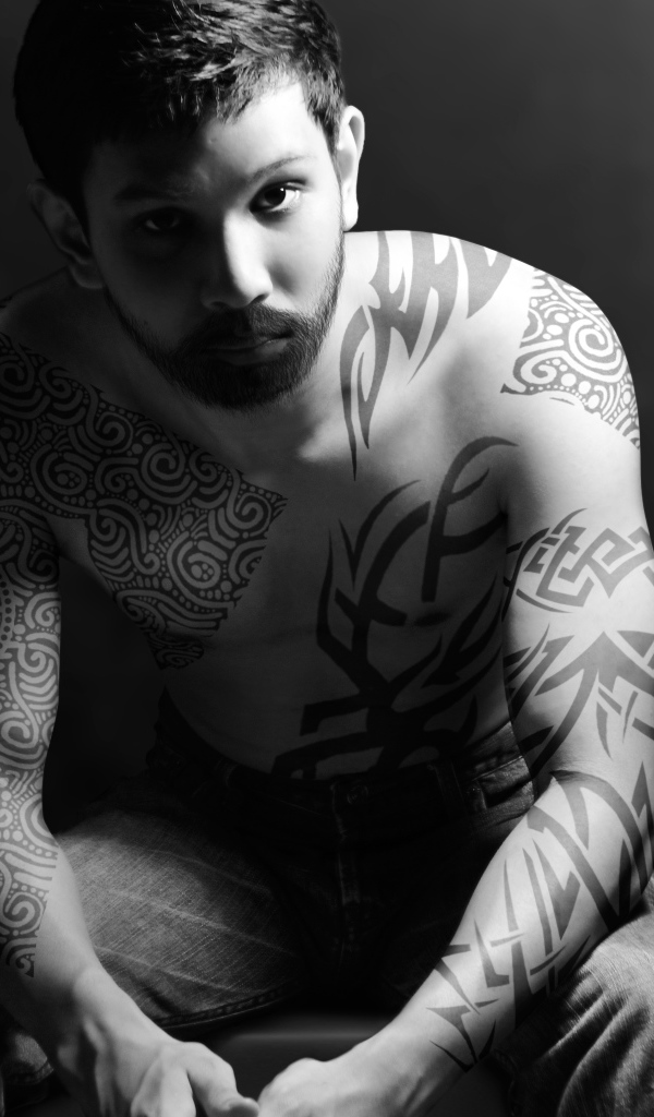 Молодой парень с татуировками на теле на сером фоне