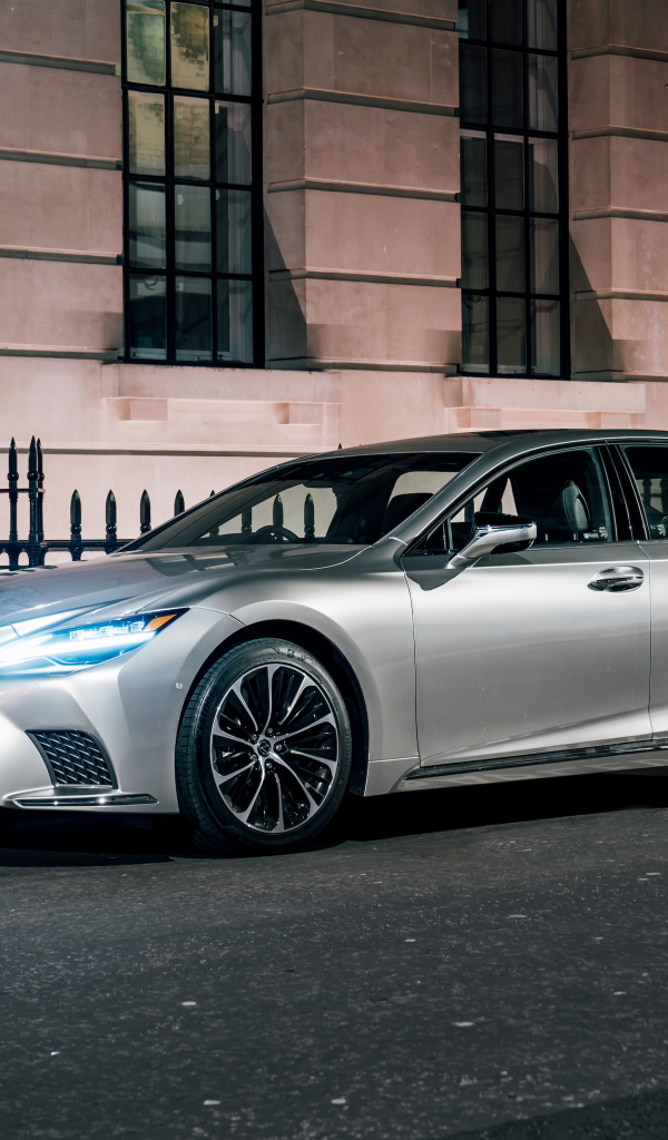 Серебристый автомобиль Lexus LS 500h 2021  года с включенными фарами