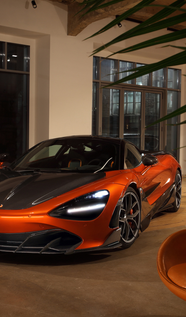 Оранжевый автомобиль  McLaren 720S у дома с креслом