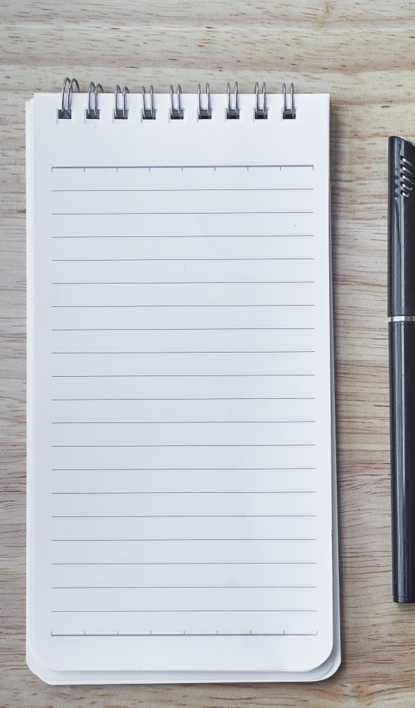 Авторучка и блокнот лежат на деревянном столе