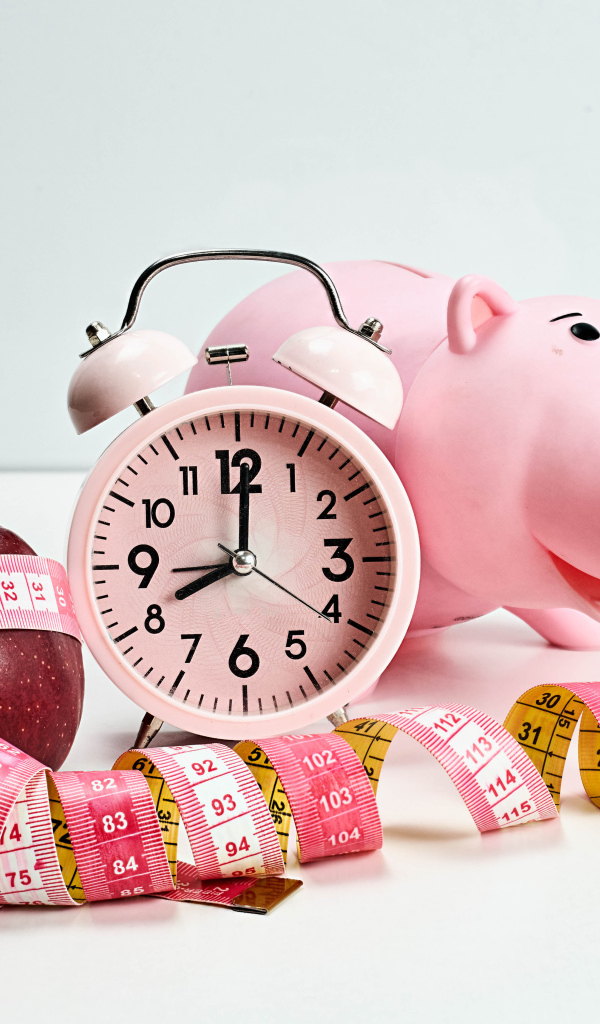 Будильник, свинья копилка, яблоко и сантиметр на белом фоне