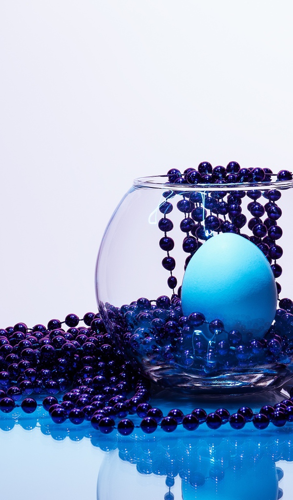 Синие бусы на столе со стеклянной вазой и яйцом