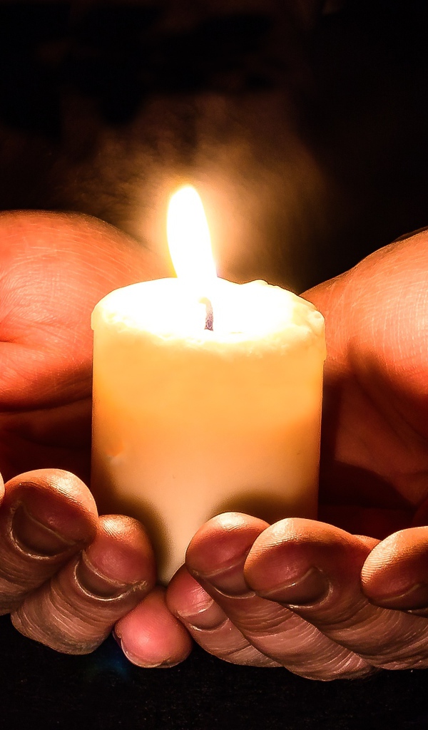 Зажженная свеча в руках на черном фоне