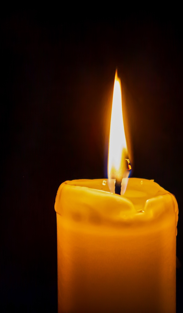 Зажженная желтая свеча на черном фоне 