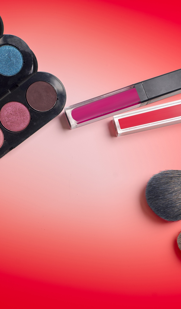 Блеск для губ, тени и кисточки на красном фоне