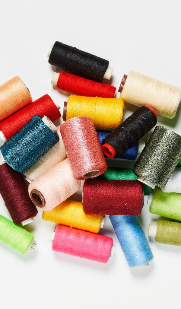 Много катушек разноцветных ниток на белом фоне 