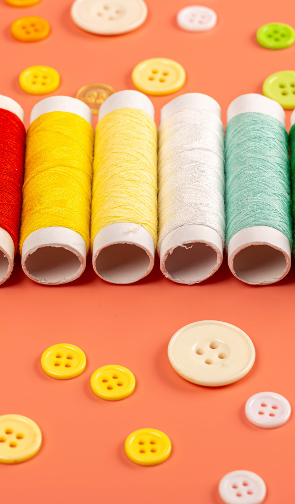 Разноцветные нитки и пуговицы на розовом фоне