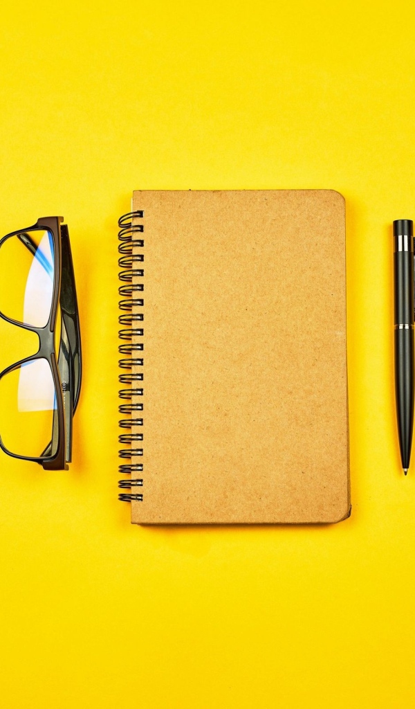 Блокнот, очки и ручка на желтом фоне