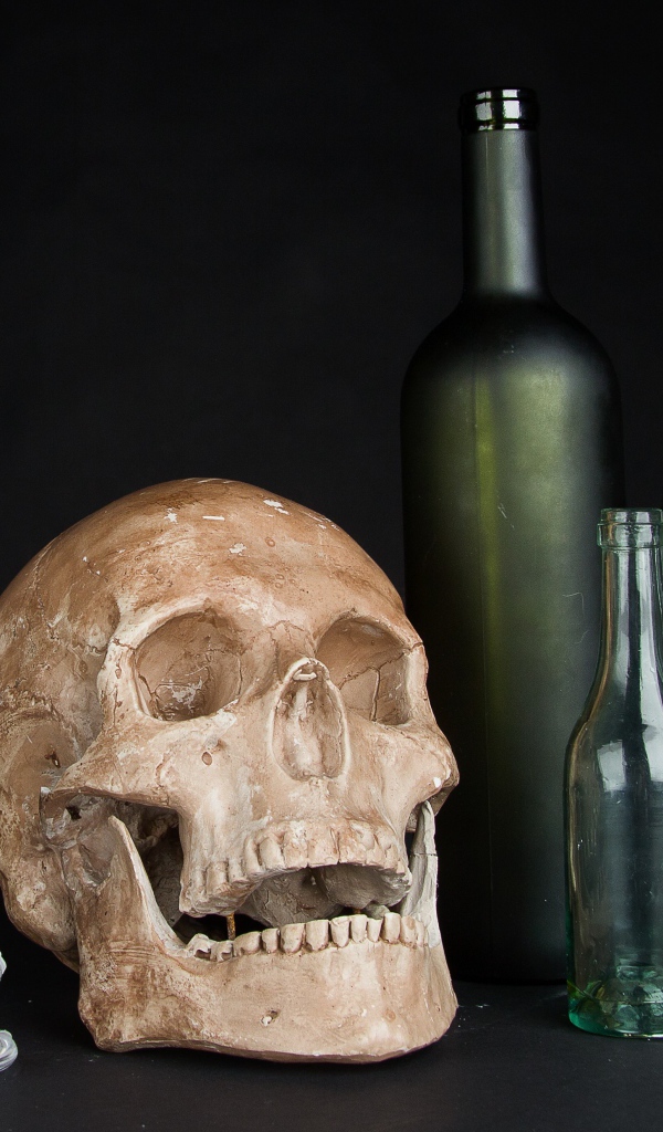 Череп, пустые бутылки и свеча на черном фоне