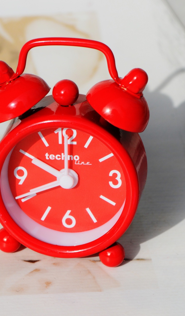 Маленький красный будильник стоит на столе 
