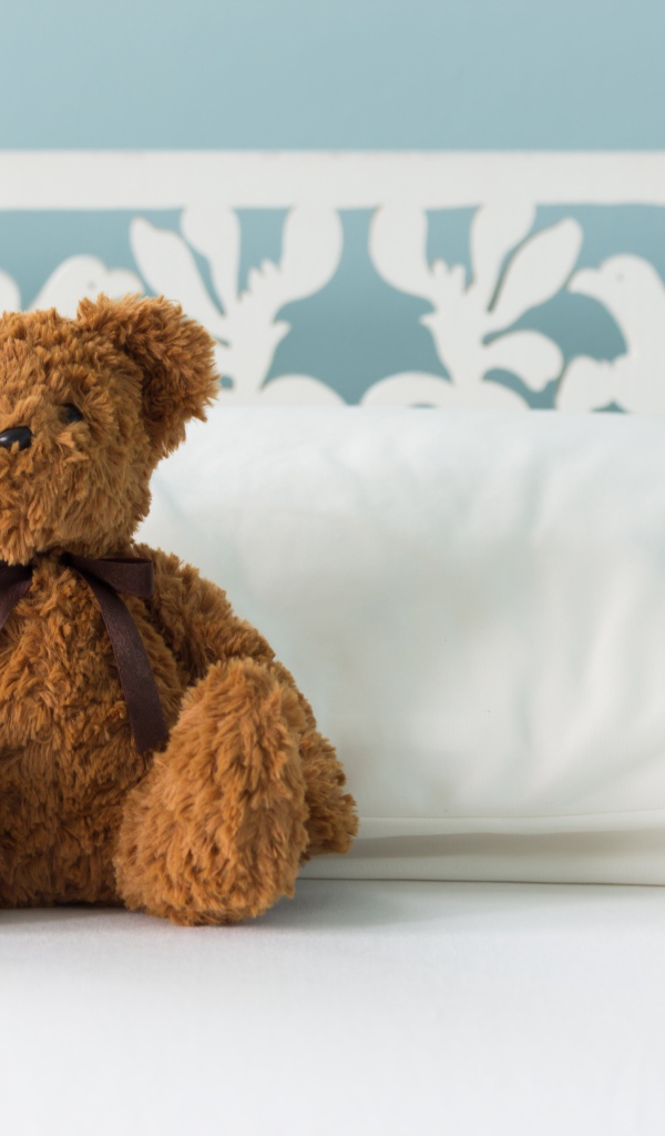 Игрушечный медвежонок сидит на белой постели