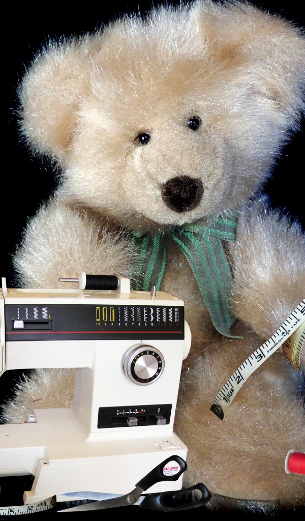 Игрушечный медвежонок со швейной машинкой на черном фоне 