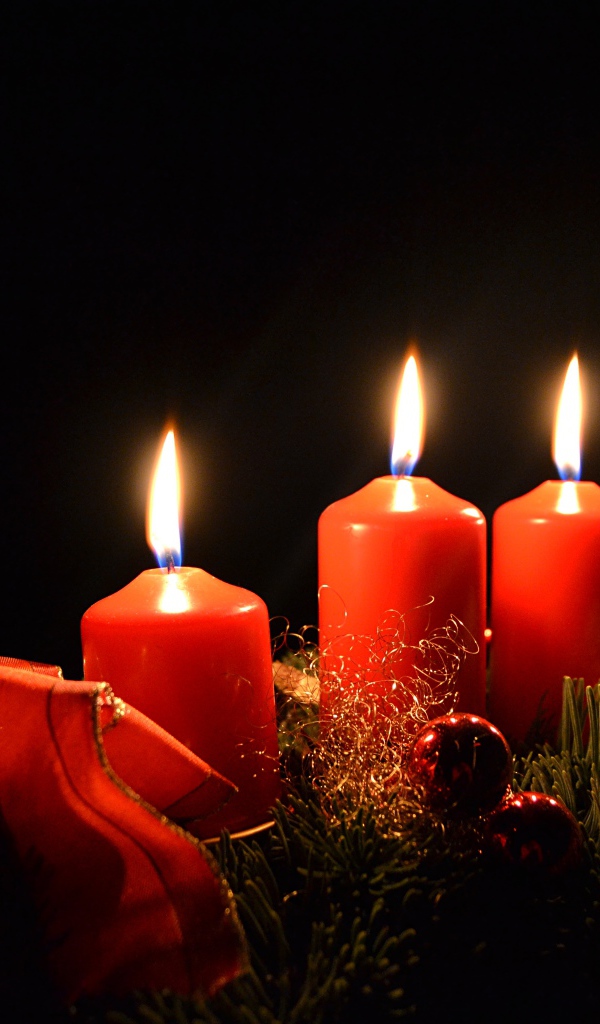 Три зажженные красные свечи с еловой веткой на черном фоне 