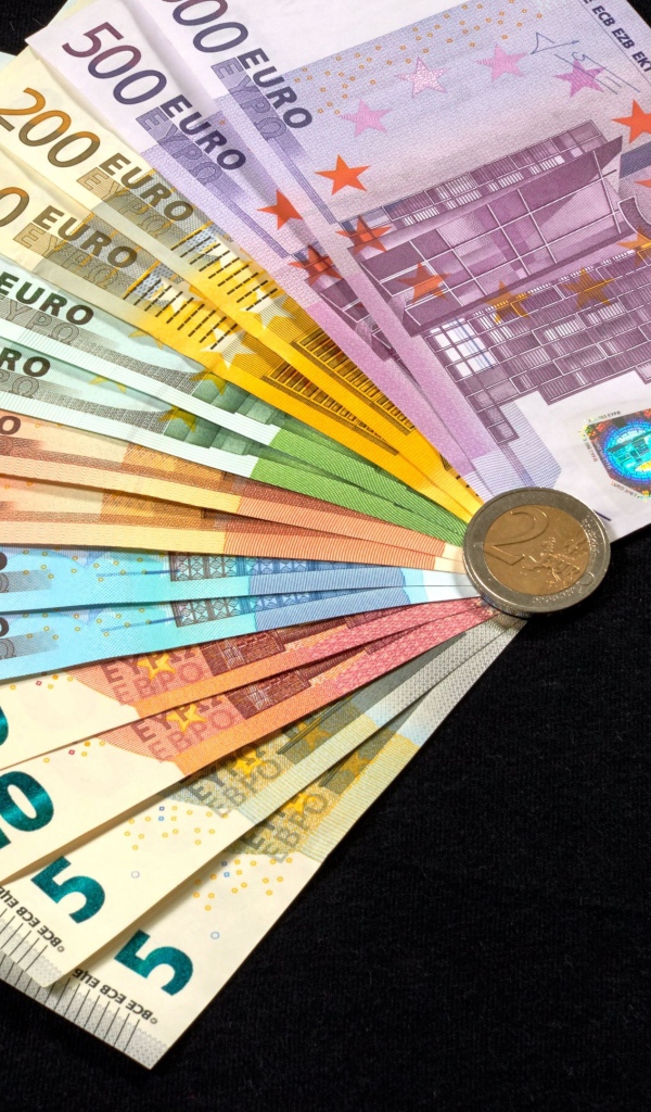 Пачка купюр евро с монетой на черном столе 