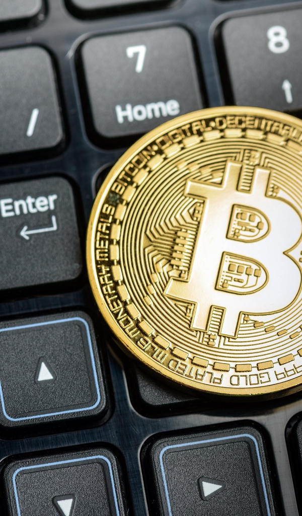 Золотая монета биткоин на черной клавиатуре