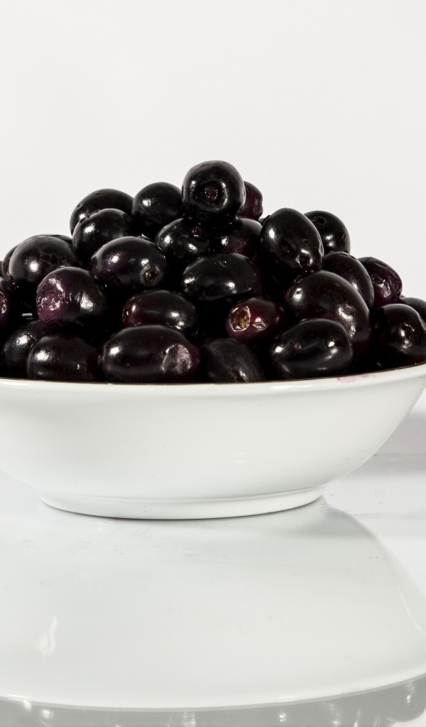 Черные оливки в белой тарелке отражаются в поверхности